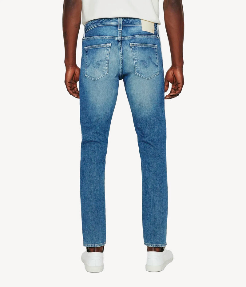 Back view of the Dylan jeans in medium indigo wash, focusing on the slim, tailored fit through the thighs and the tapered leg opening. The faded and whiskered details give the jeans a well-worn yet polished appearance.