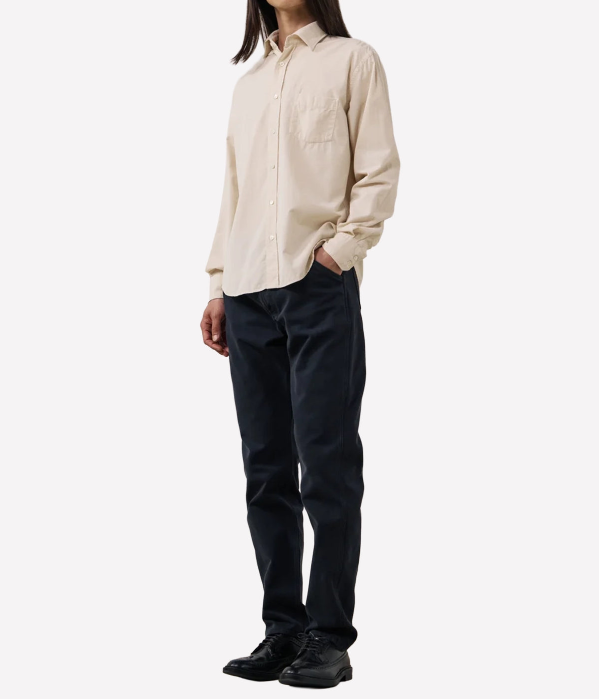 A model wearing a light beige long-sleeve button-down shirt and dark navy pants, standing against a plain white studio background.