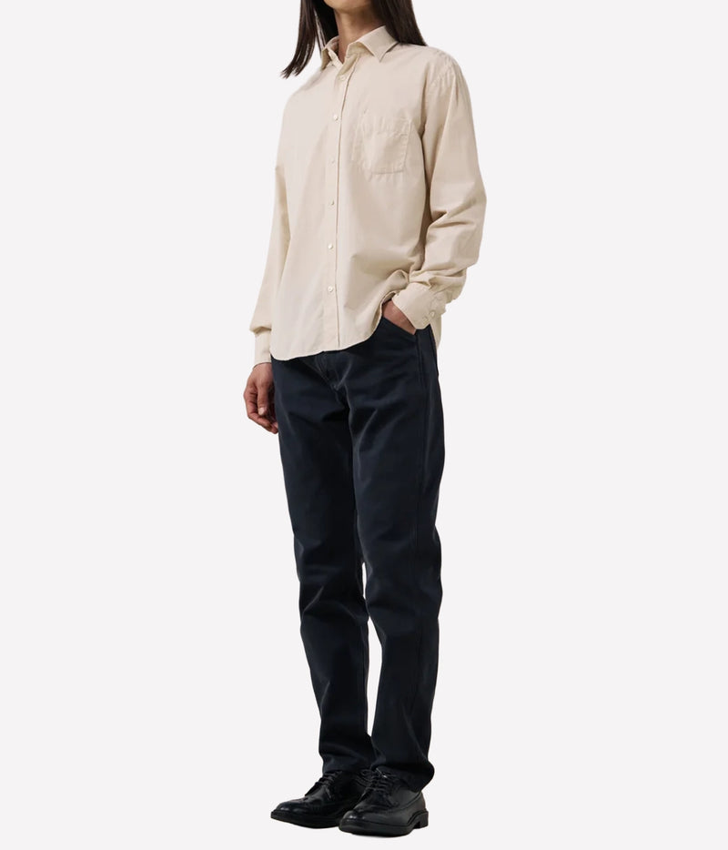 A model wearing a light beige long-sleeve button-down shirt and dark navy pants, standing against a plain white studio background.