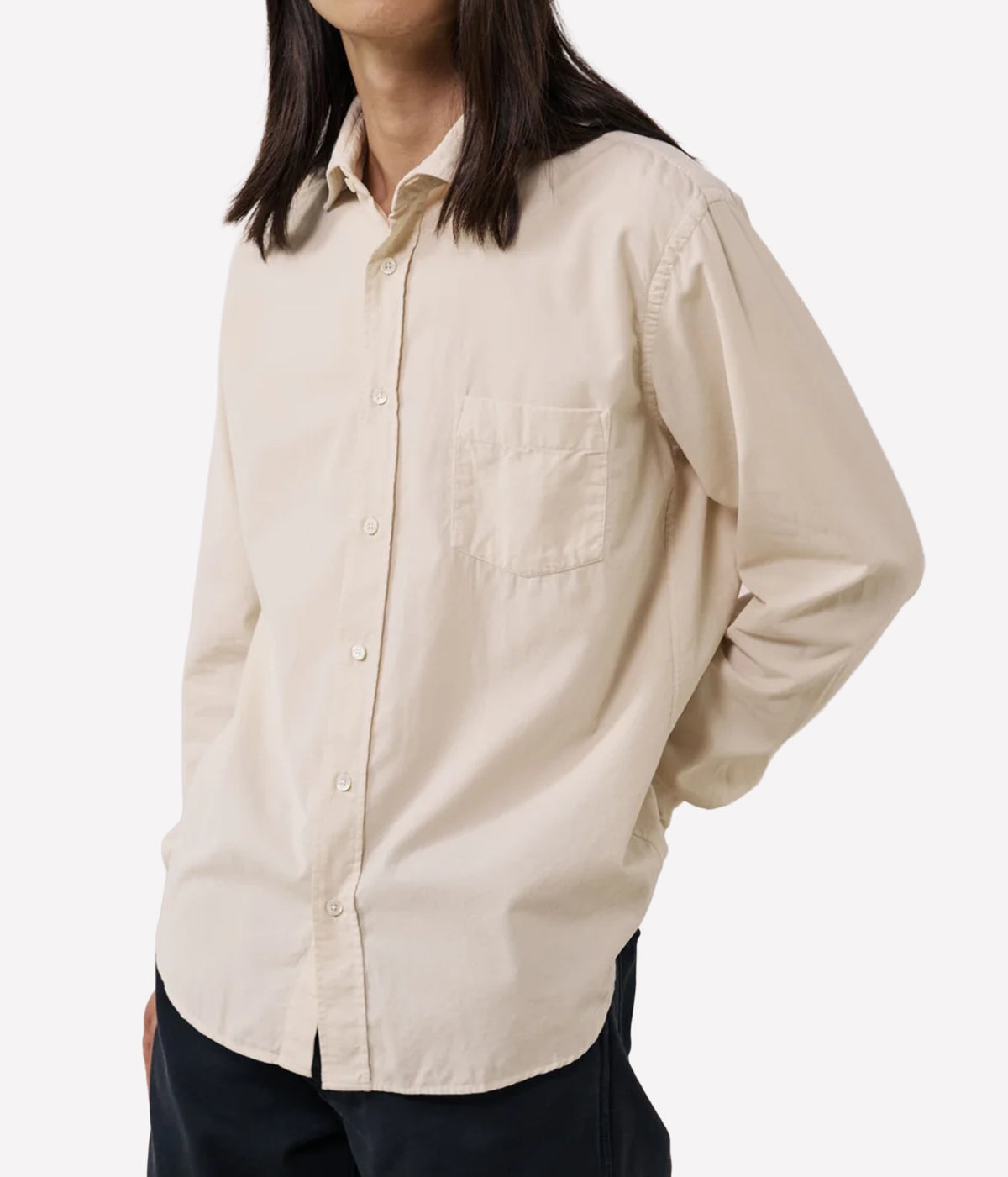 A person wearing a light beige long-sleeve button-up shirt with a chest pocket, paired with dark pants, against a plain light grey background.