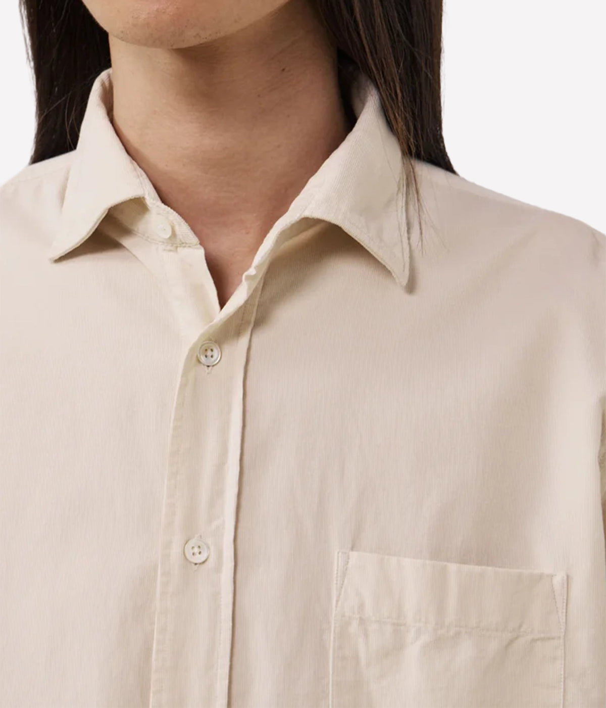Close-up of a person wearing a light beige or cream button-up shirt with a pointed collar and a chest pocket, against a plain light background.