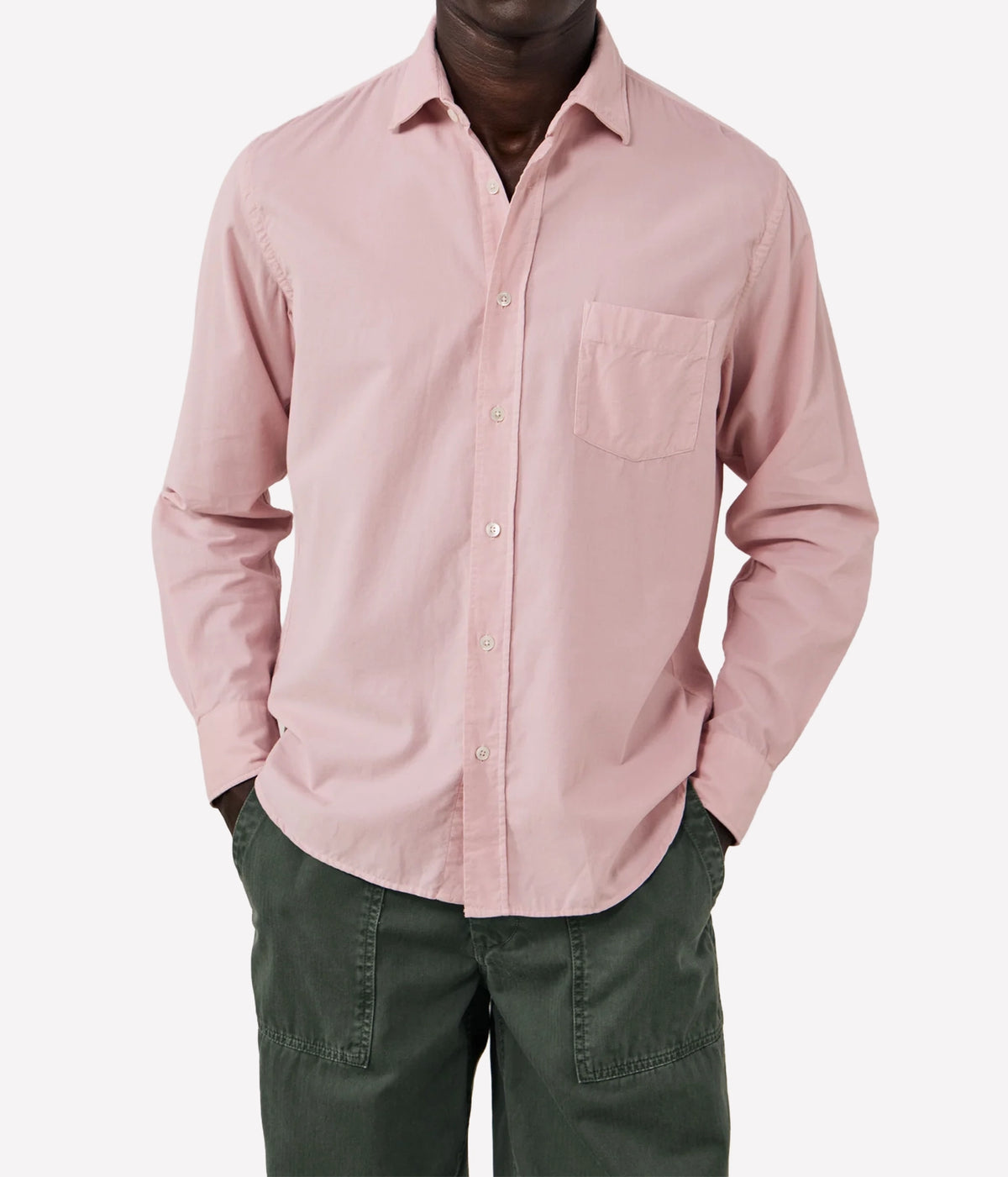 A man wearing a dusty pink long-sleeve button-down shirt with a chest pocket, paired with dark green pants, shown against a plain light grey background.