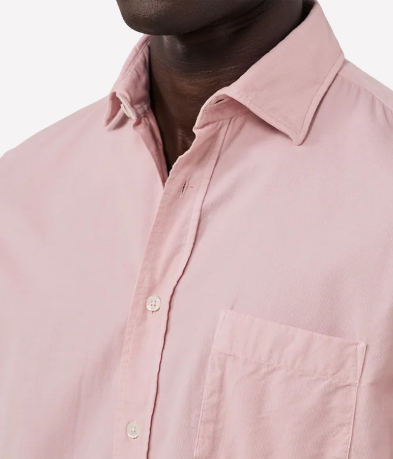 Close-up of a man wearing a light pink button-down shirt, showing the collar, chest pocket, and front buttons against a plain light background.