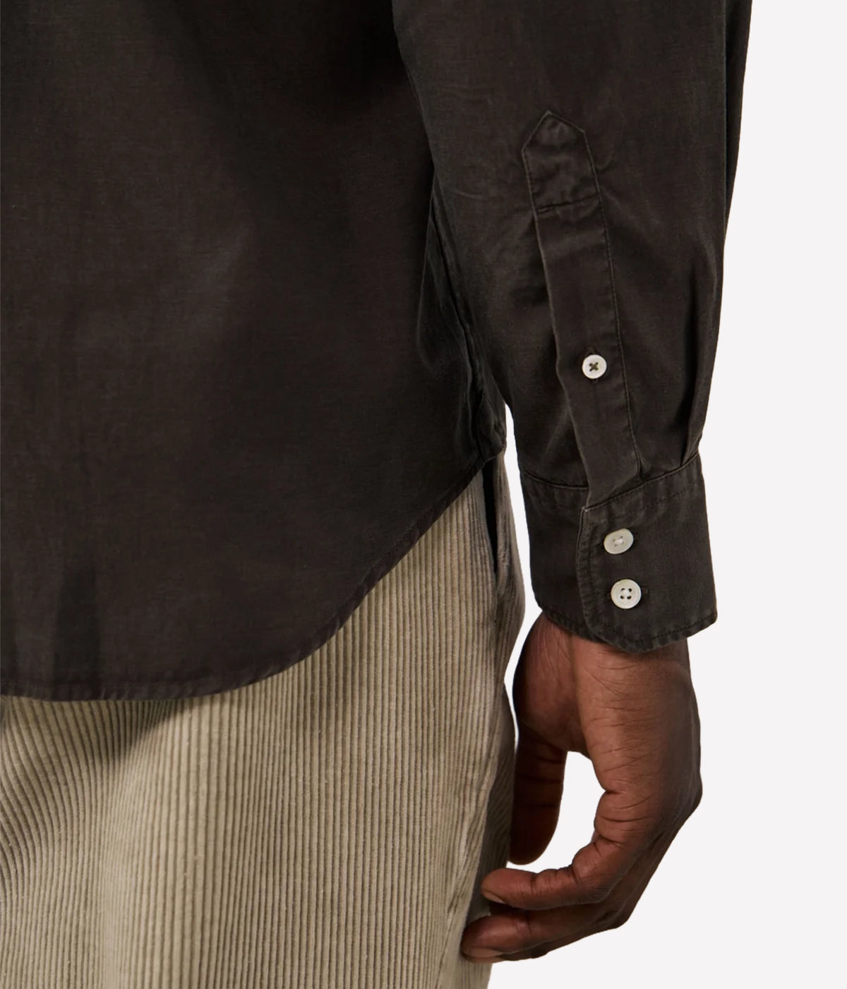 Close-up of a person wearing a dark brown long-sleeve button-up shirt with beige pinstriped trousers, showing the sleeve cuff with three buttons and the hand.