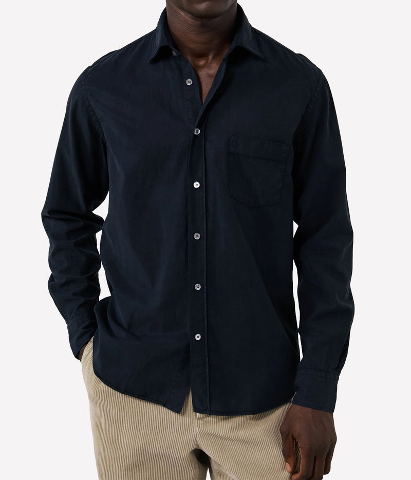 A man wearing a dark navy blue long-sleeve button-down shirt with a chest pocket, paired with beige corduroy trousers, shown against a plain light grey background.