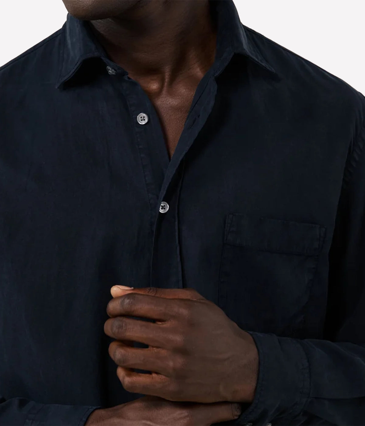 Close-up of a man wearing a dark navy long-sleeve button-up shirt with a chest pocket, shown against a light grey background.