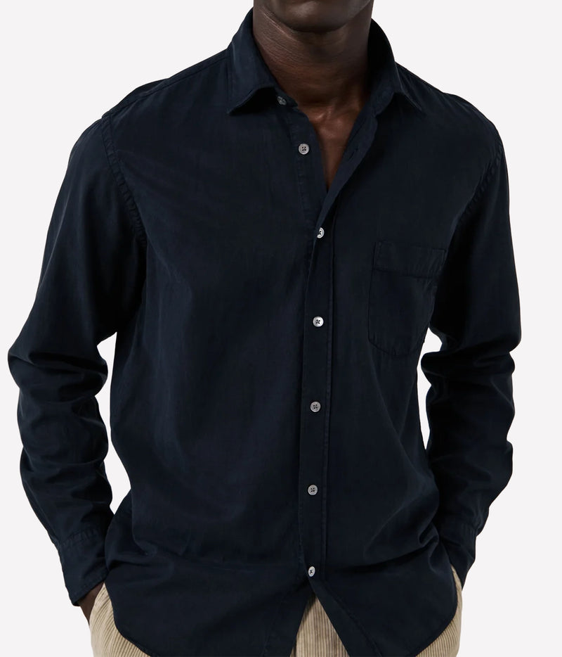 A man wearing a dark navy long-sleeve button-up shirt with a chest pocket, paired with beige trousers, shown against a light grey background.