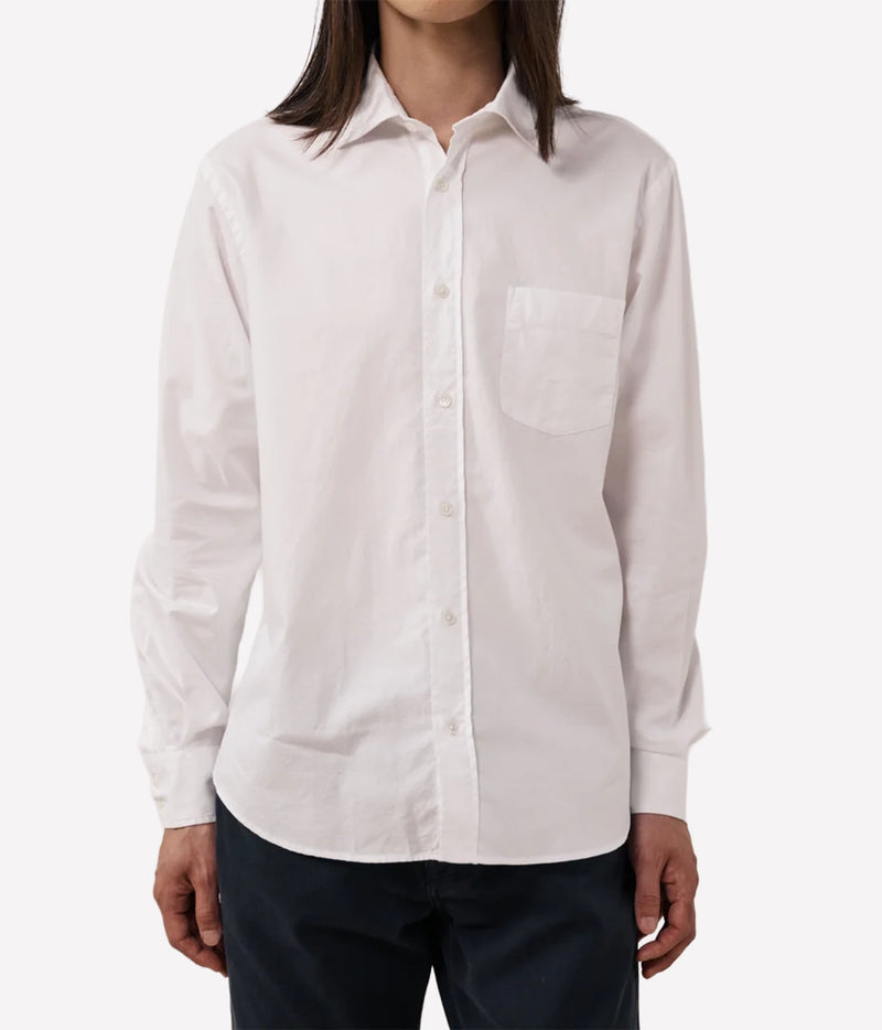A man wearing a white long-sleeve button-down shirt with a single chest pocket, paired with dark pants.
