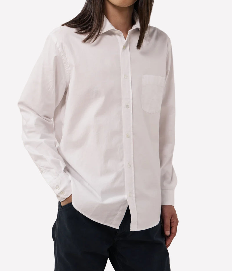 A man wearing a white long-sleeve button-up shirt with a single chest pocket, paired with dark pants.