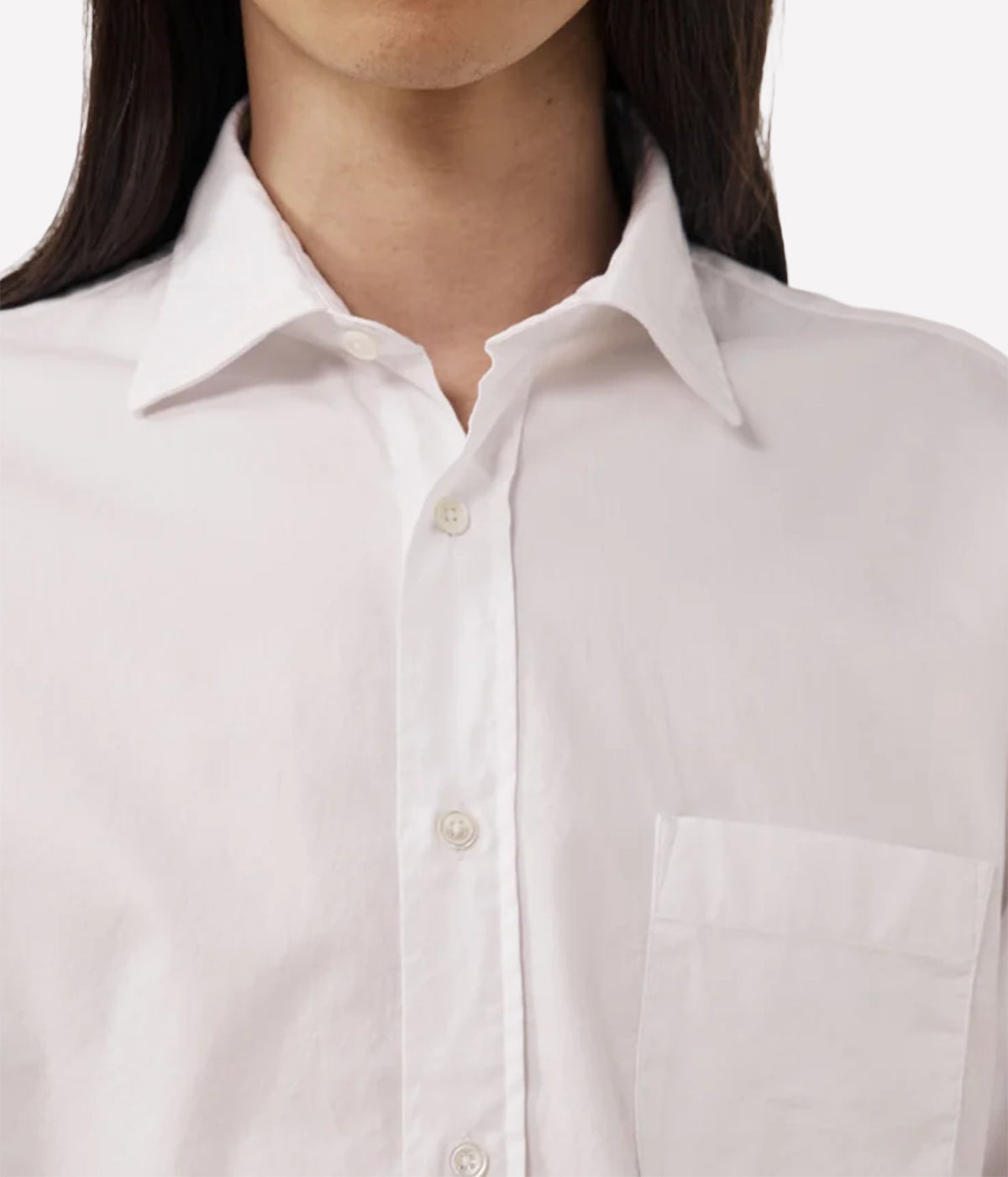 Close-up of a person wearing a white long-sleeve button-down shirt with a pointed collar and a chest pocket, against a plain light background.