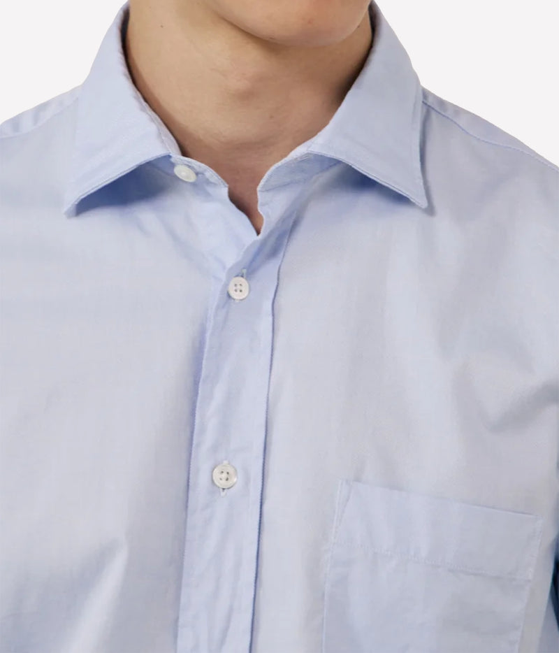 Close-up of a light blue button-down shirt worn by a model, showing the collar, front buttons, and chest pocket.