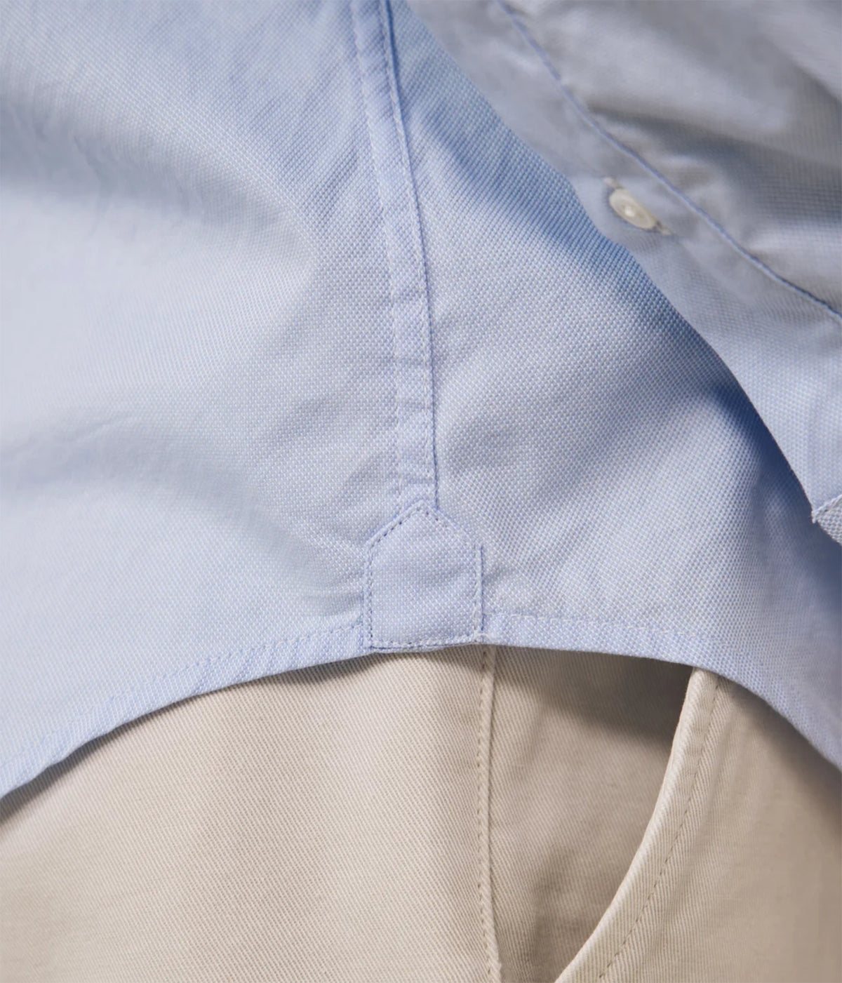 Close-up detail of a light blue button-up shirt layered over a beige garment, showing the fabric texture and stitching.