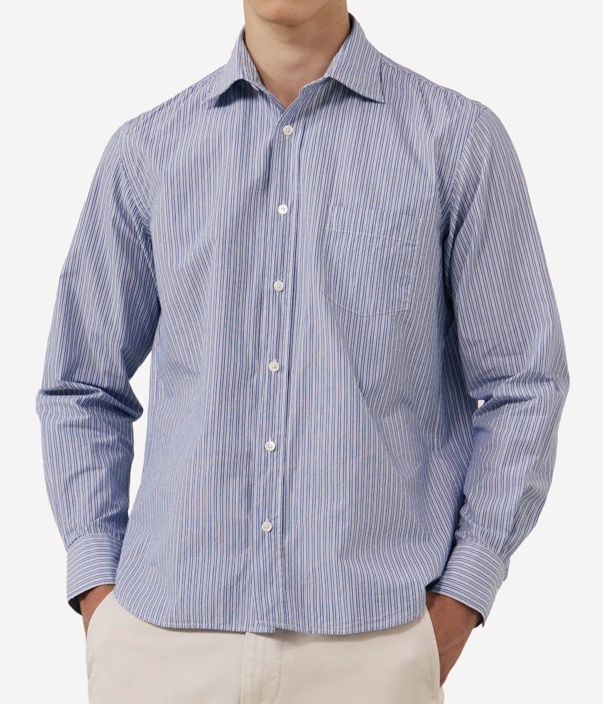 A man wearing a blue and white vertically striped long-sleeve button-down shirt with a chest pocket, paired with light beige trousers.