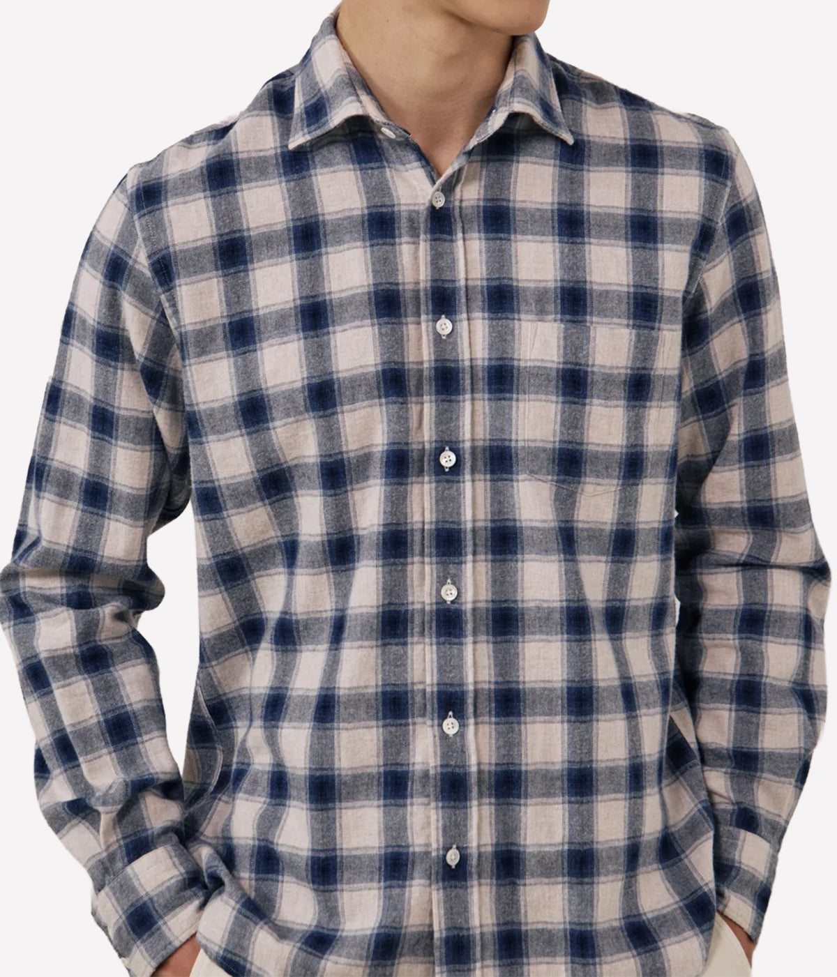 A man wearing a long-sleeve button-up plaid shirt in navy blue and beige, shown from the neck down against a light grey background.