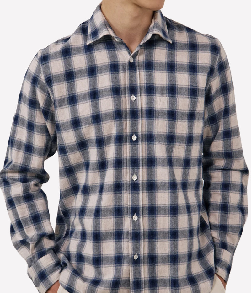 A man wearing a long-sleeve button-up plaid shirt in navy blue and beige, shown from the neck down against a light grey background.