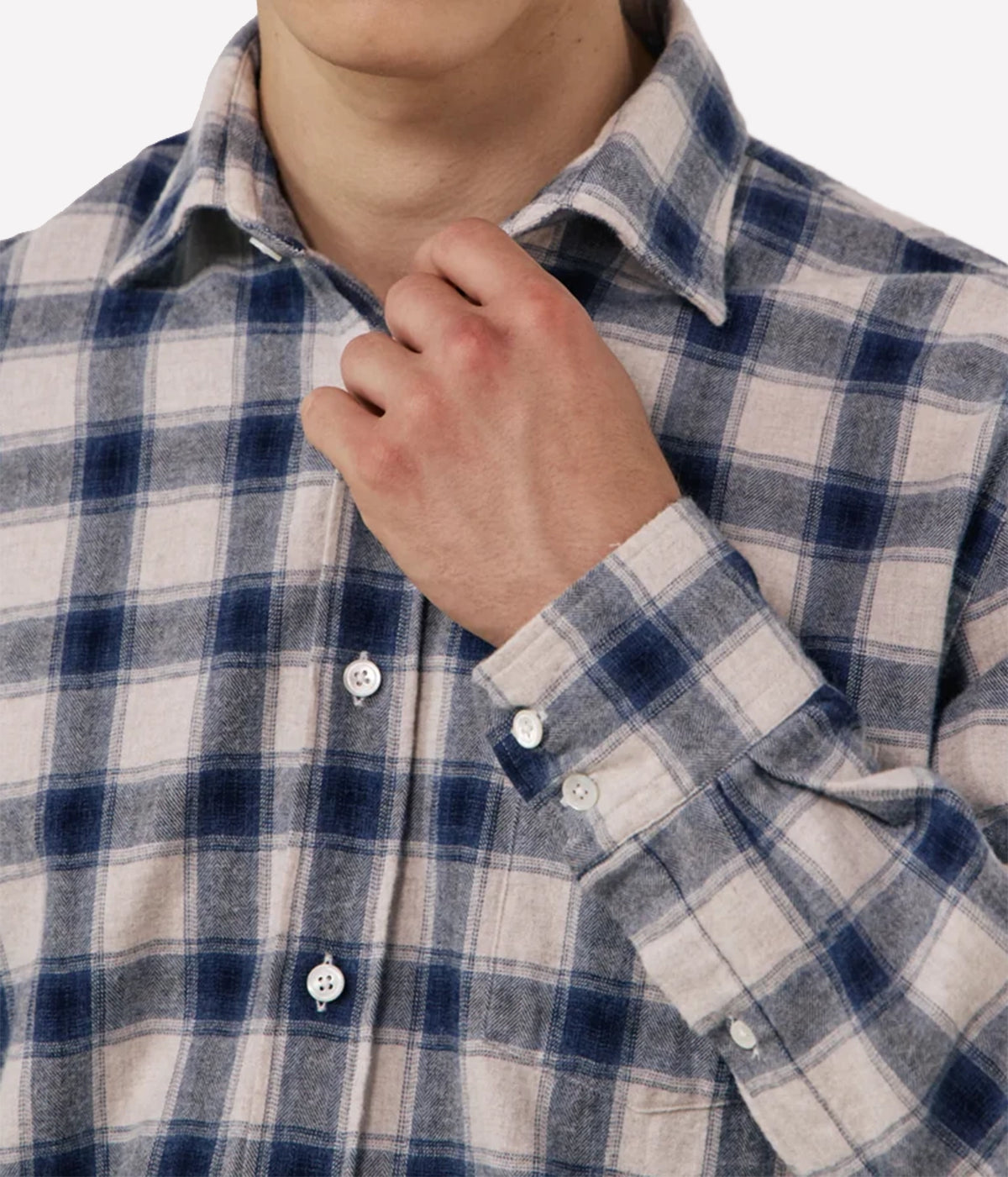Close-up of a person wearing a long-sleeve plaid button-up shirt in blue, navy, and off-white, with the hand adjusting the collar.