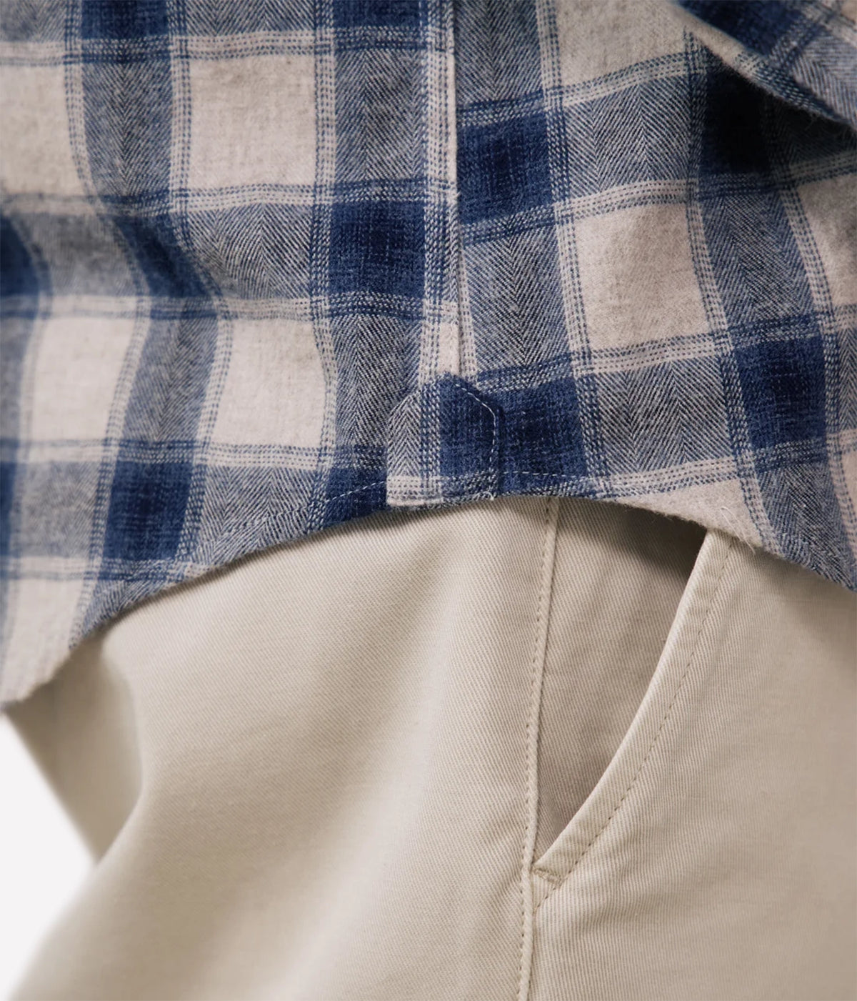 Close-up of a blue and beige plaid flannel shirt layered over light beige trousers, showing the fabric texture and a button detail.