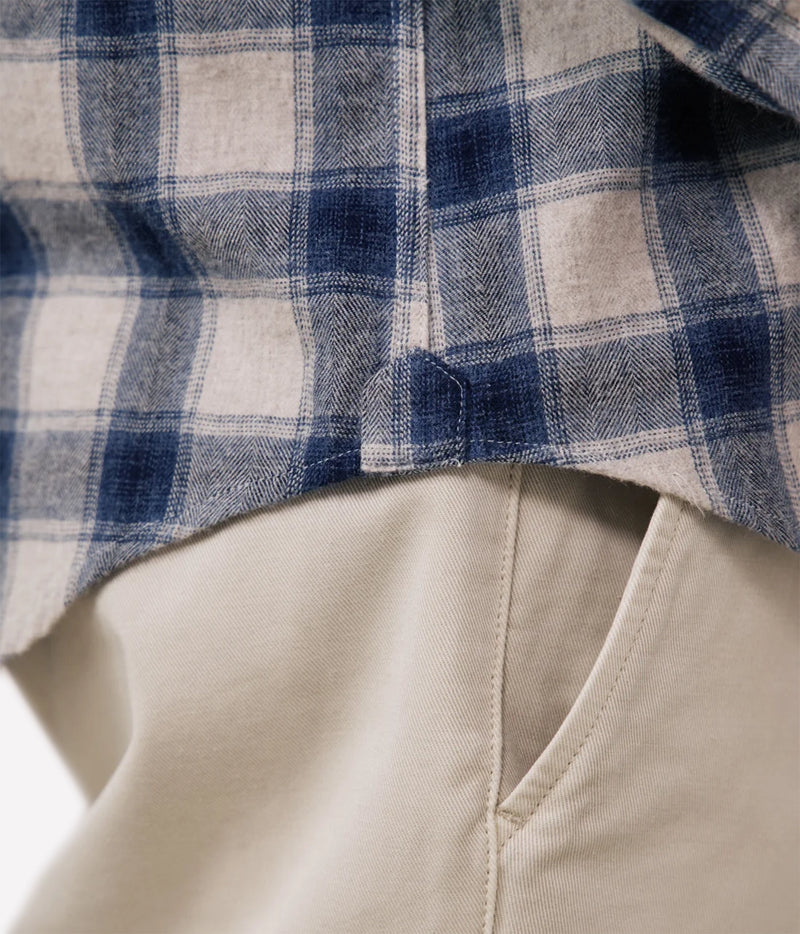 Close-up of a blue and beige plaid flannel shirt layered over light beige trousers, showing the fabric texture and a button detail.