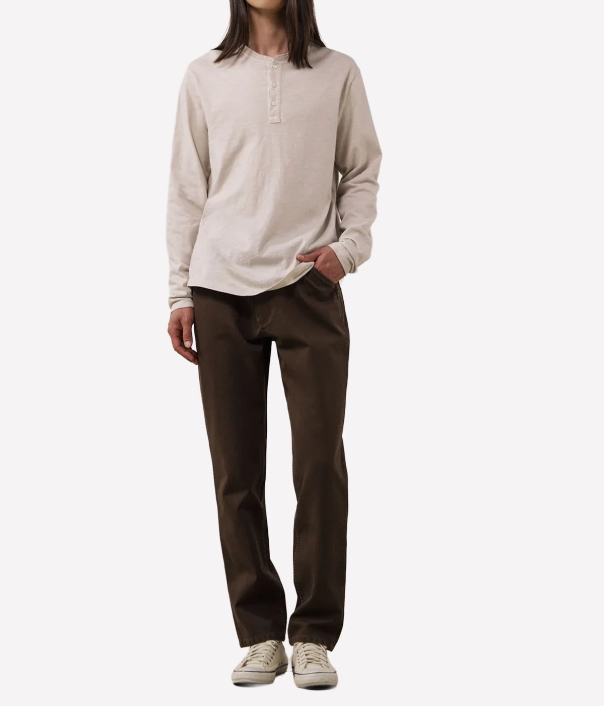 A model wearing a light beige long-sleeve henley shirt and dark brown straight-leg pants, paired with beige sneakers, against a plain white background.