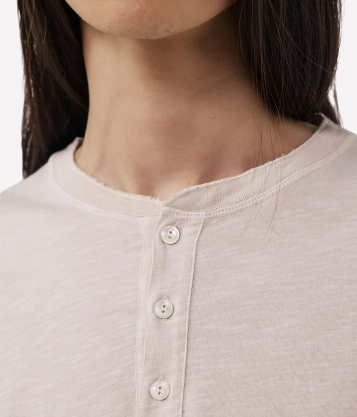 Close-up of a person wearing a light beige or cream Henley shirt with a three-button placket.