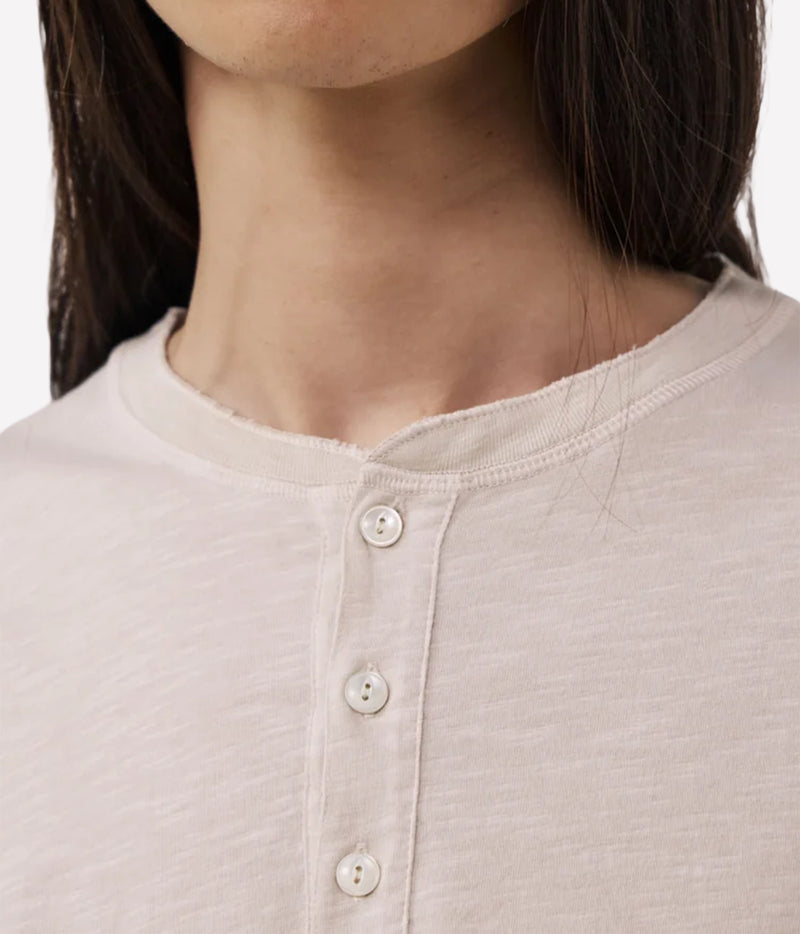 Close-up of a person wearing a light beige or cream Henley shirt with a three-button placket.
