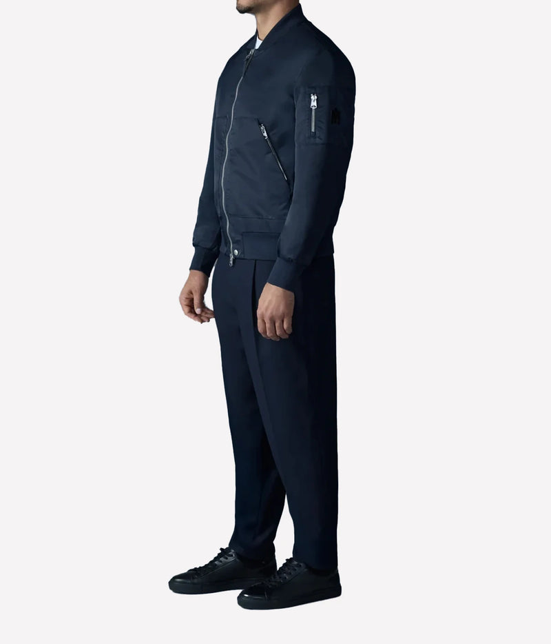 A man shown in side profile wearing a dark navy blue zip-up bomber jacket and matching navy pants with black sneakers, against a light gray studio background.