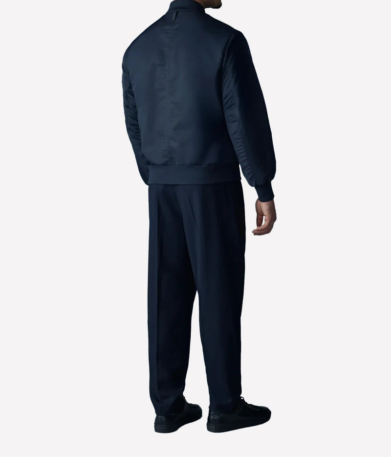 A man wearing a dark navy blue tracksuit, viewed from the back, standing against a light gray background.