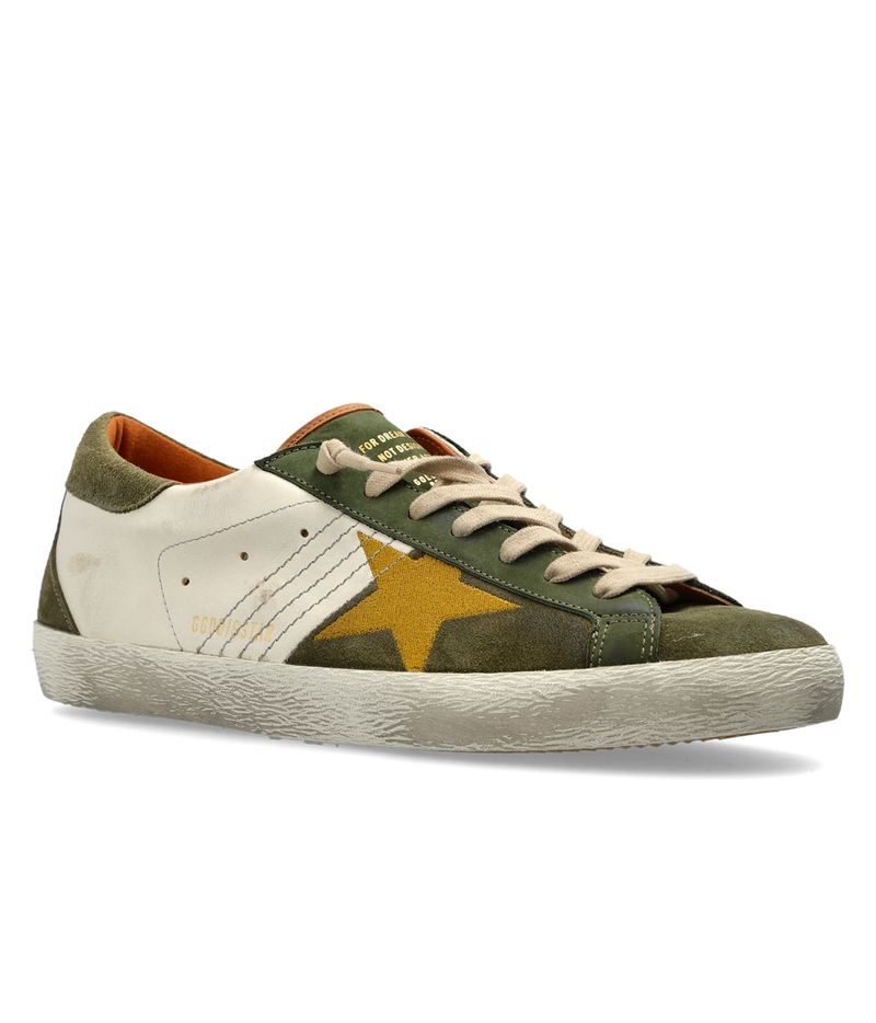 A low-top sneaker featuring distressed olive green suede, off-white leather panels, a prominent gold star on the side, and beige laces, shown against a plain white background.