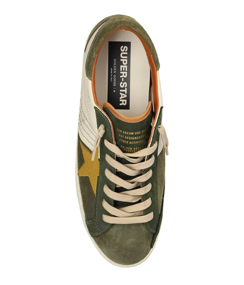 A top-down view of a Golden Goose Super-Star sneaker in olive green suede and cream canvas, featuring a gold star on the side, cream laces, and a black and white 'SUPER-STAR' label on the tongue.