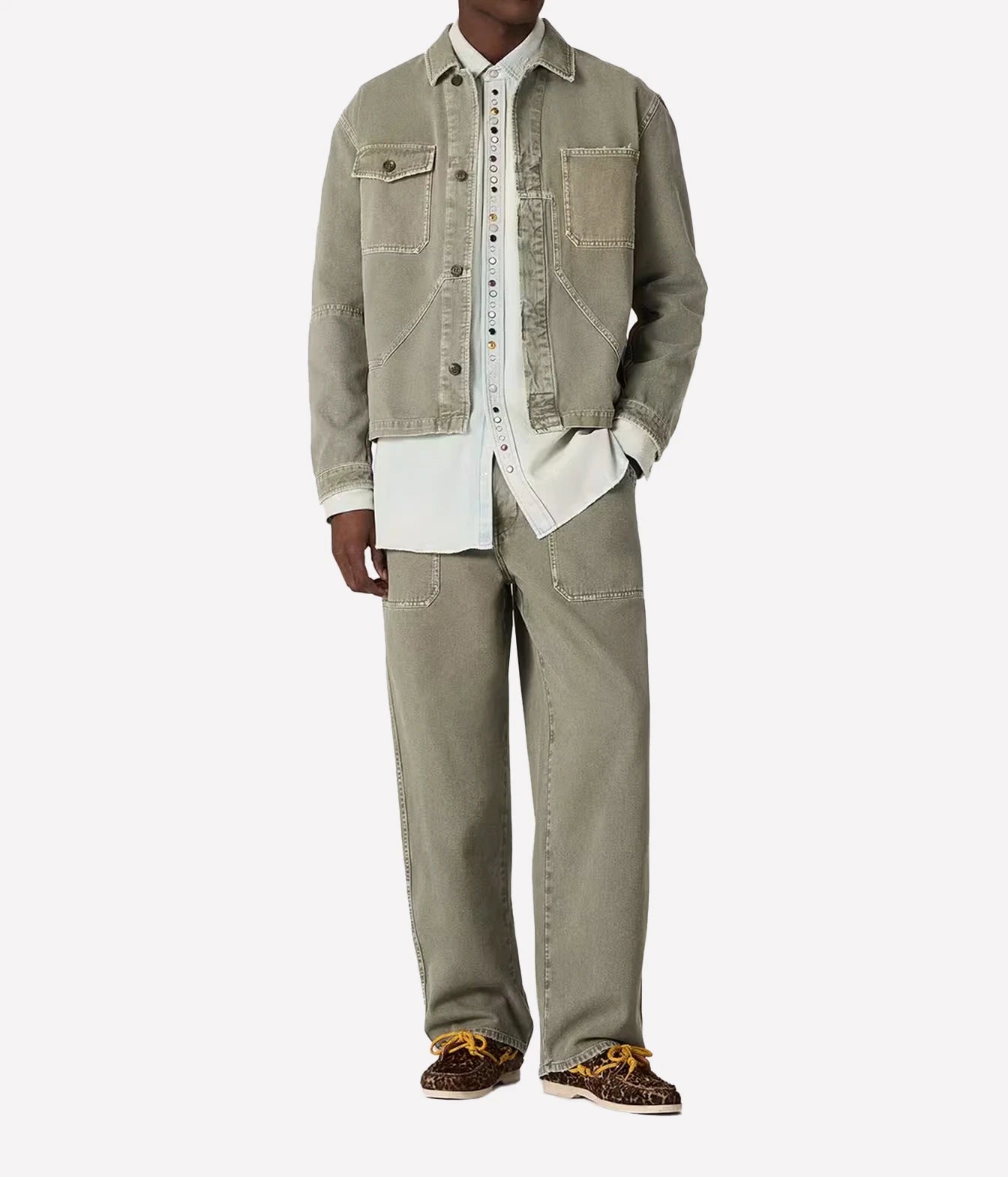 A model wearing a light olive green denim jacket and matching wide-leg jeans over a white button-up shirt, paired with leopard print sneakers, on a light gray background.