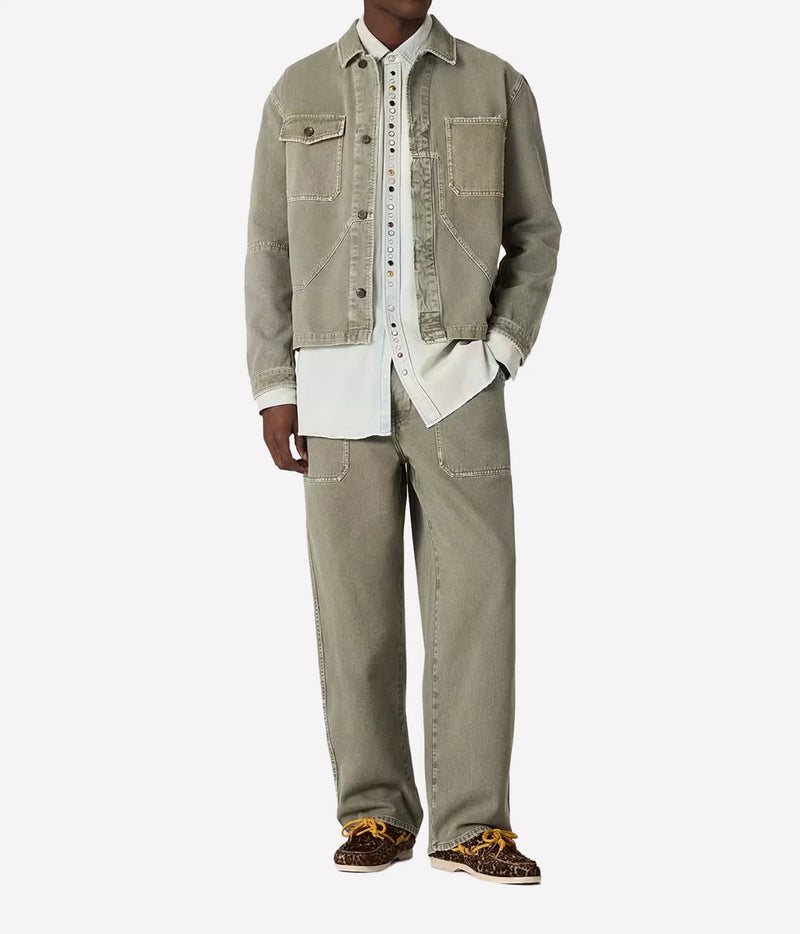 A model wearing a light olive green denim jacket and matching wide-leg jeans over a white button-up shirt, paired with leopard print sneakers, on a light gray background.