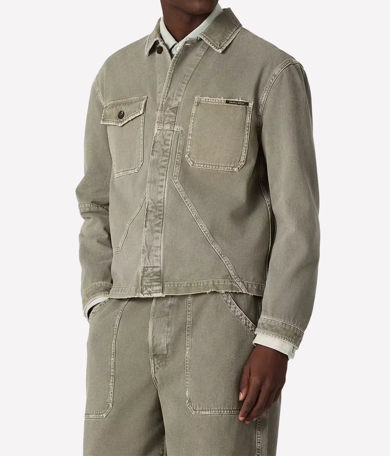 A cropped sage green denim work jacket with contrast stitching, worn by a model with matching denim pants against a light gray background.