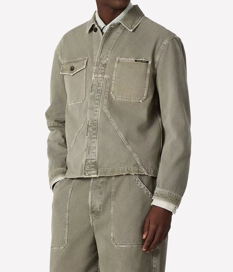 A cropped sage green denim work jacket with contrast stitching, worn by a model with matching denim pants against a light gray background.