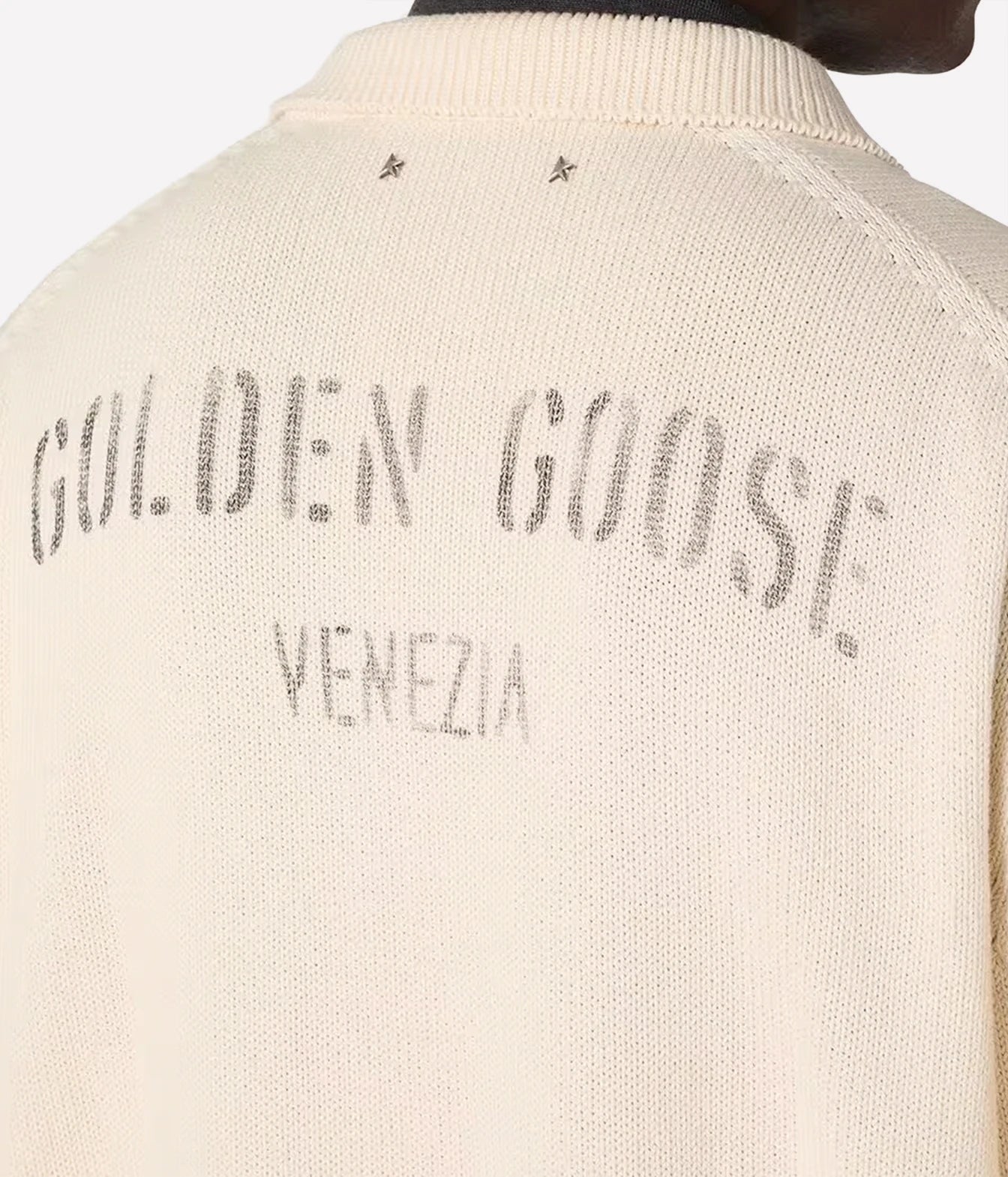 Close-up of the back of a cream-colored knit sweater with 'GOLDEN GOOSE VENEZIA' printed in a faded gray tone across the upper back.
