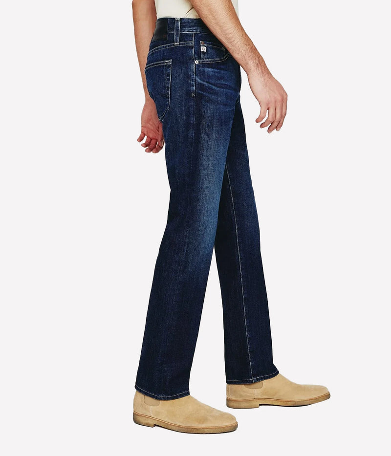 AG Graduate slim straight jeans for men in a medium-dark wash, featuring a slim mid-rise waist and relaxed fit through the hip to the knee. Tapered leg opening with Flex 360° Denim for added comfort and stretch