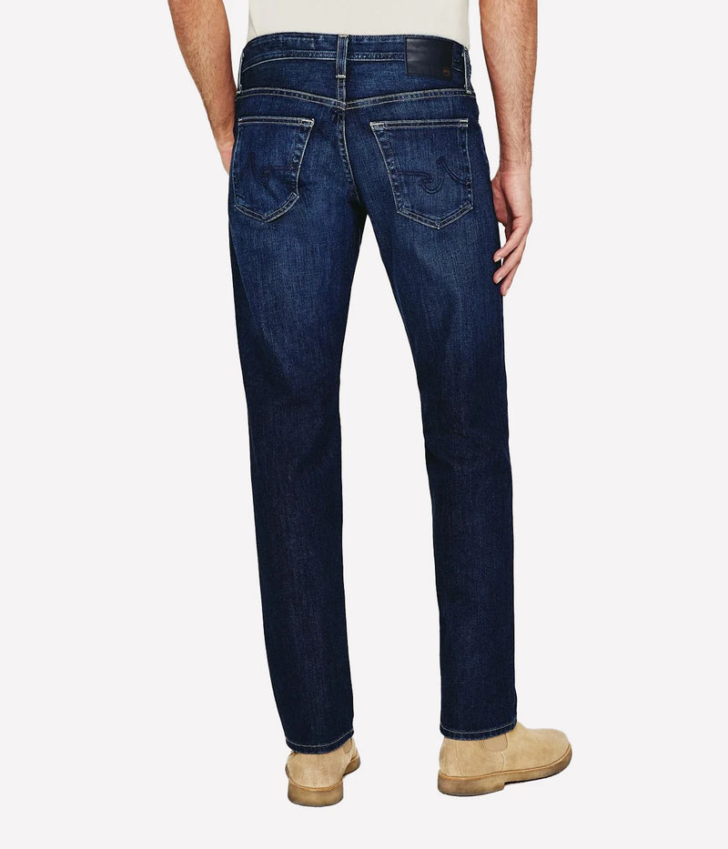 AG Graduate slim straight jeans for men in a medium-dark wash, featuring a slim mid-rise waist and relaxed fit through the hip to the knee. Tapered leg opening with Flex 360° Denim for added comfort and stretch