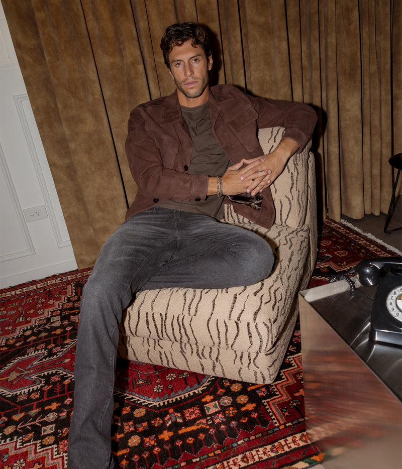 Man wearing Lardini Suede Jacket in Brown with blue jeans, seated in an armchair, full-length front view