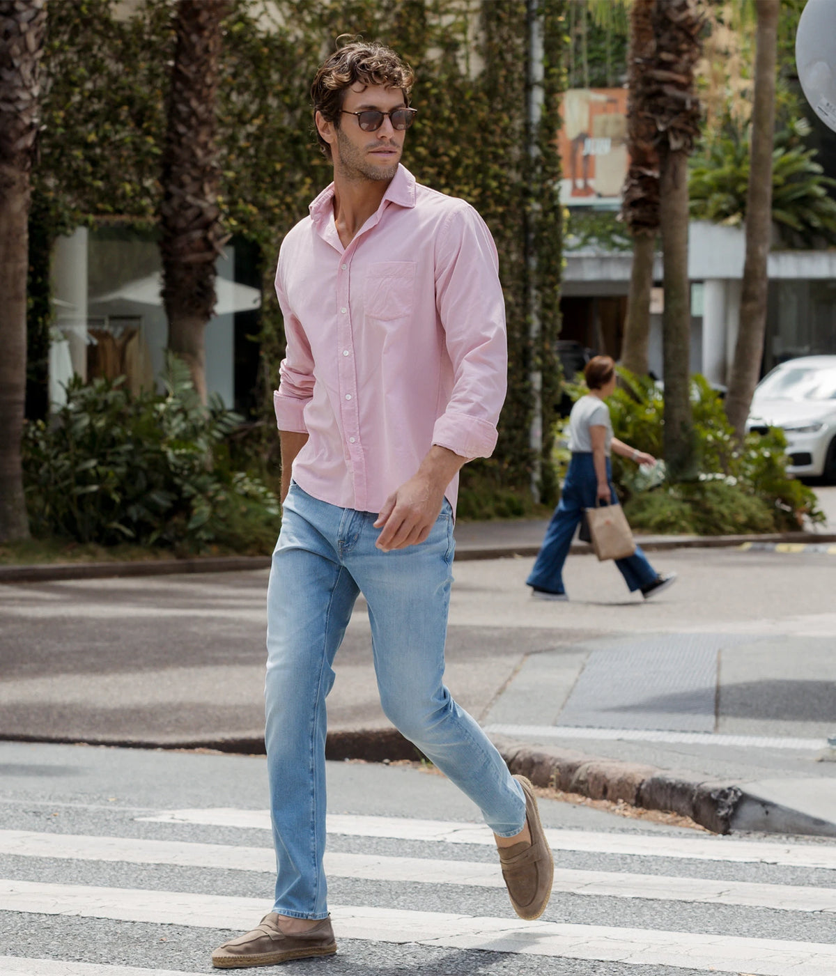 Man wearing Hartford Paul Fine Corduroy Shirt in Old Pink with light blue jeans and brown shoes, crossing the street, full-length front view
