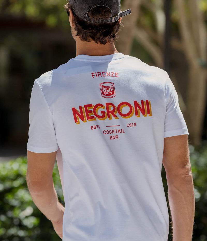 Back view of man wearing The Refined Spirit Negroni Cocktail Bar Tee in White with a cap, outdoors