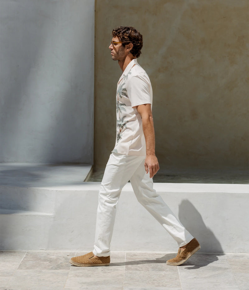 Man wearing Mavrans Palm Row Weekend Shirt in Light Green with white trousers and loafers, walking, side view