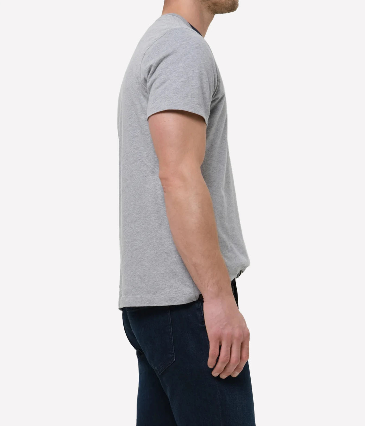 A man shown from the side wearing a light grey short-sleeve crewneck t-shirt and dark blue jeans, photographed against a clean white background.