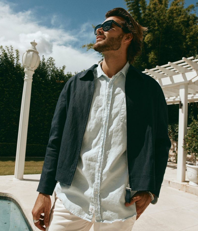 Man wearing a tan Lardini linen jacket with a zip front, elasticated hem and cuffs, and a shirt collar, styled with a white tee and white trousers.