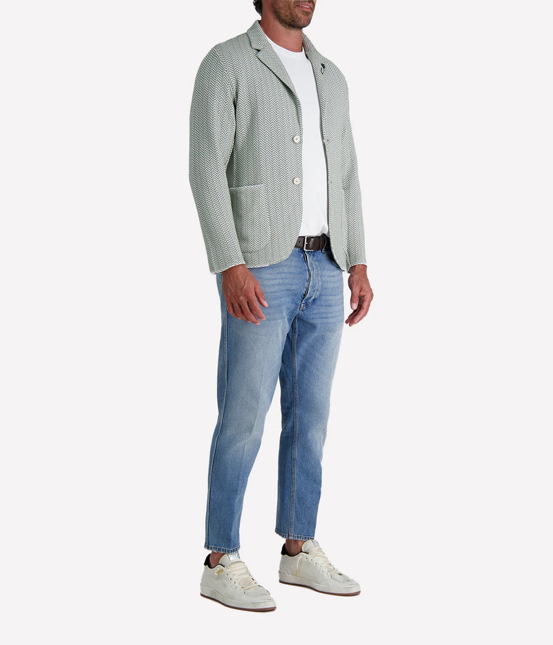 A green and white Lardini knit jacket with a herringbone pattern, soft unstructured fit, and signature floral lapel pin, made from 100% cotton, styled with a white t-shirt and jeans.