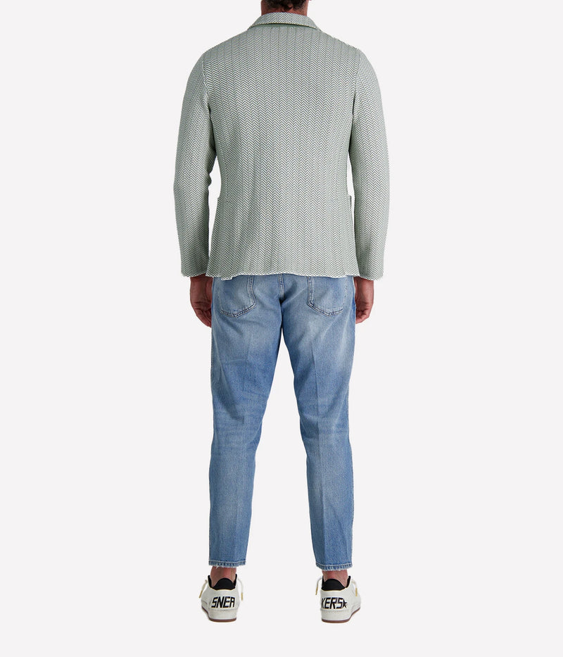 A green and white Lardini knit jacket with a herringbone pattern, soft unstructured fit, and signature floral lapel pin, made from 100% cotton, styled with a white t-shirt and jeans.
