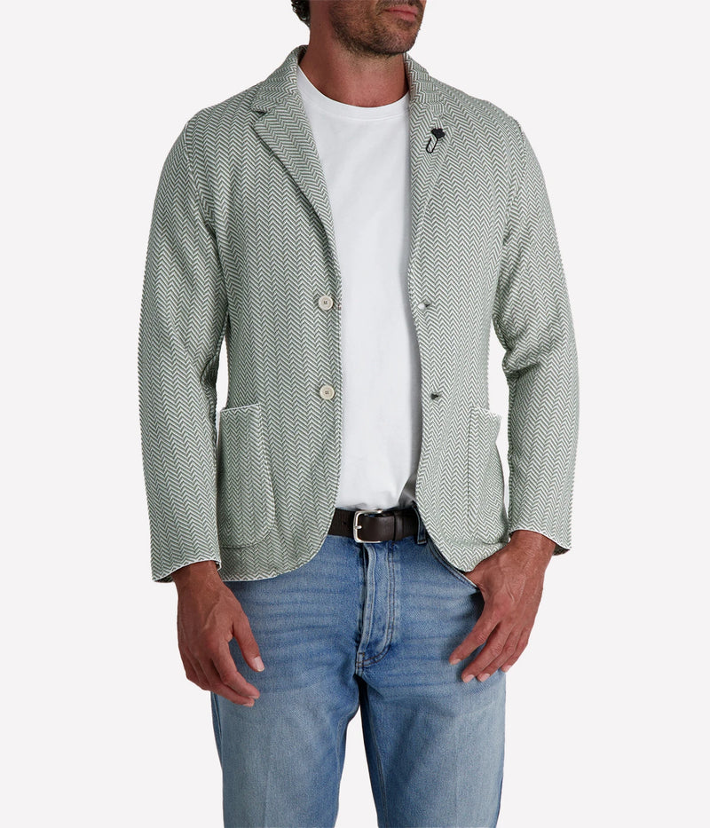 A green and white Lardini knit jacket with a herringbone pattern, soft unstructured fit, and signature floral lapel pin, made from 100% cotton, styled with a white t-shirt and jeans.