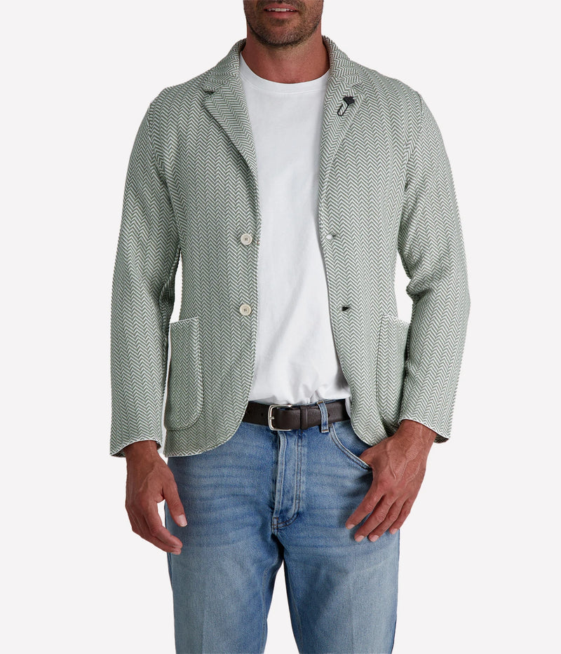 A green and white Lardini knit jacket with a herringbone pattern, soft unstructured fit, and signature floral lapel pin, made from 100% cotton, styled with a white t-shirt and jeans.