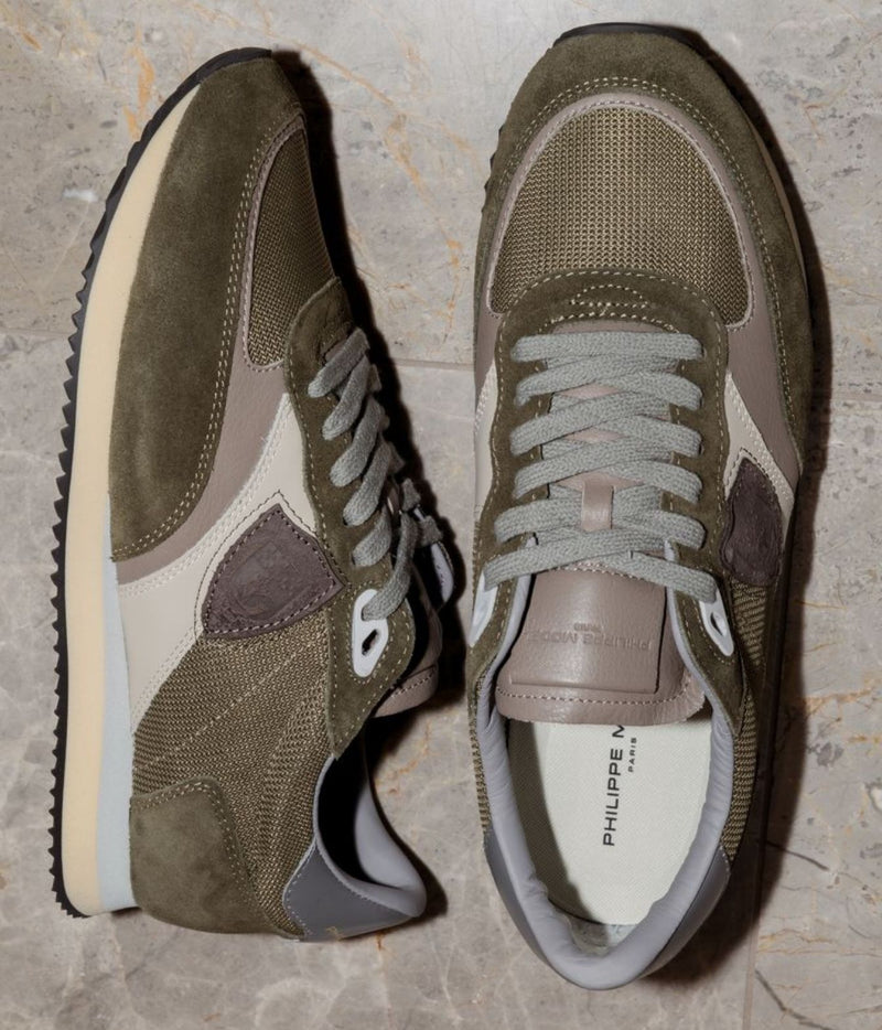 A pair of low-top sneakers in olive green, beige, and gray, shown from both side and top-down angles on a light gray marble floor. The brand name 'PHILIPPE LEBITOUR' is visible on the insole.