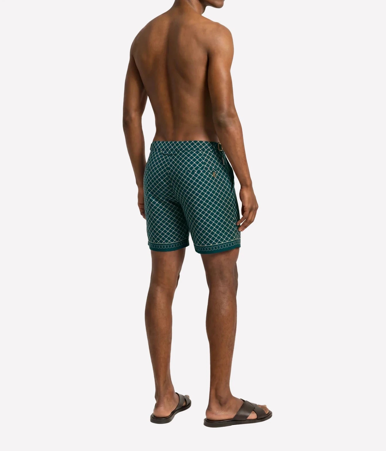A man shown from the back wearing green and white patterned swim trunks, photographed against a plain light gray studio background.