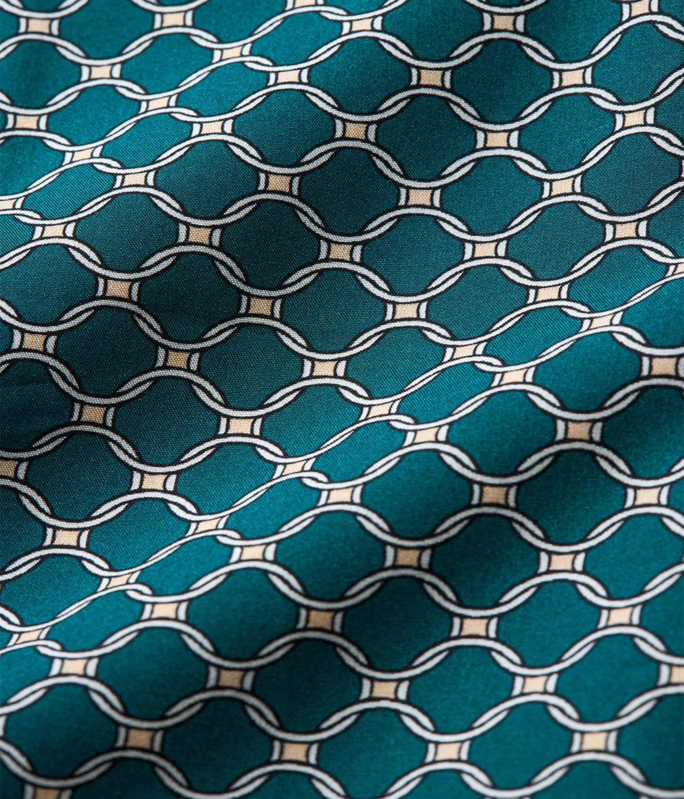 A close-up of a teal fabric with a repeating geometric chain-link pattern outlined in white and small beige accents.