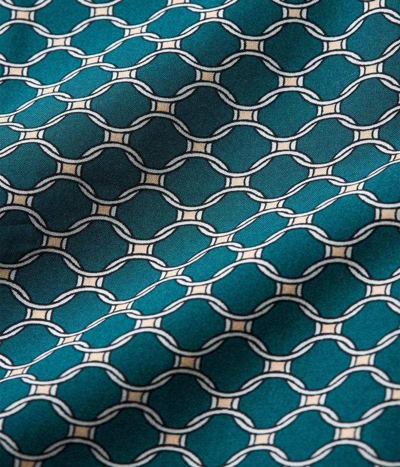 A close-up of a teal fabric with a repeating geometric chain-link pattern outlined in white and small beige accents.
